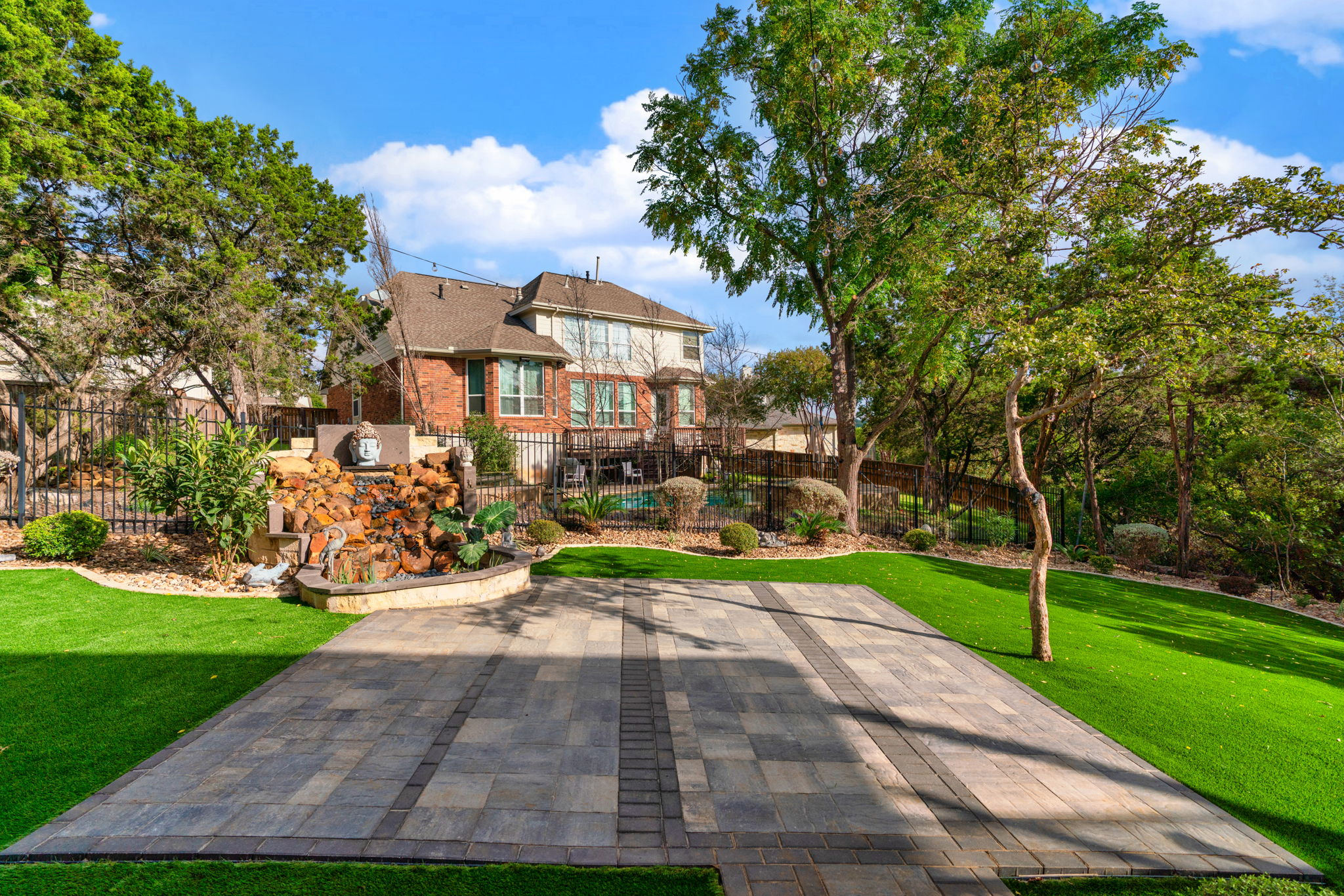 a large fenced-in backyard with a square paver patio on a landscaped lawn with a zen garden
