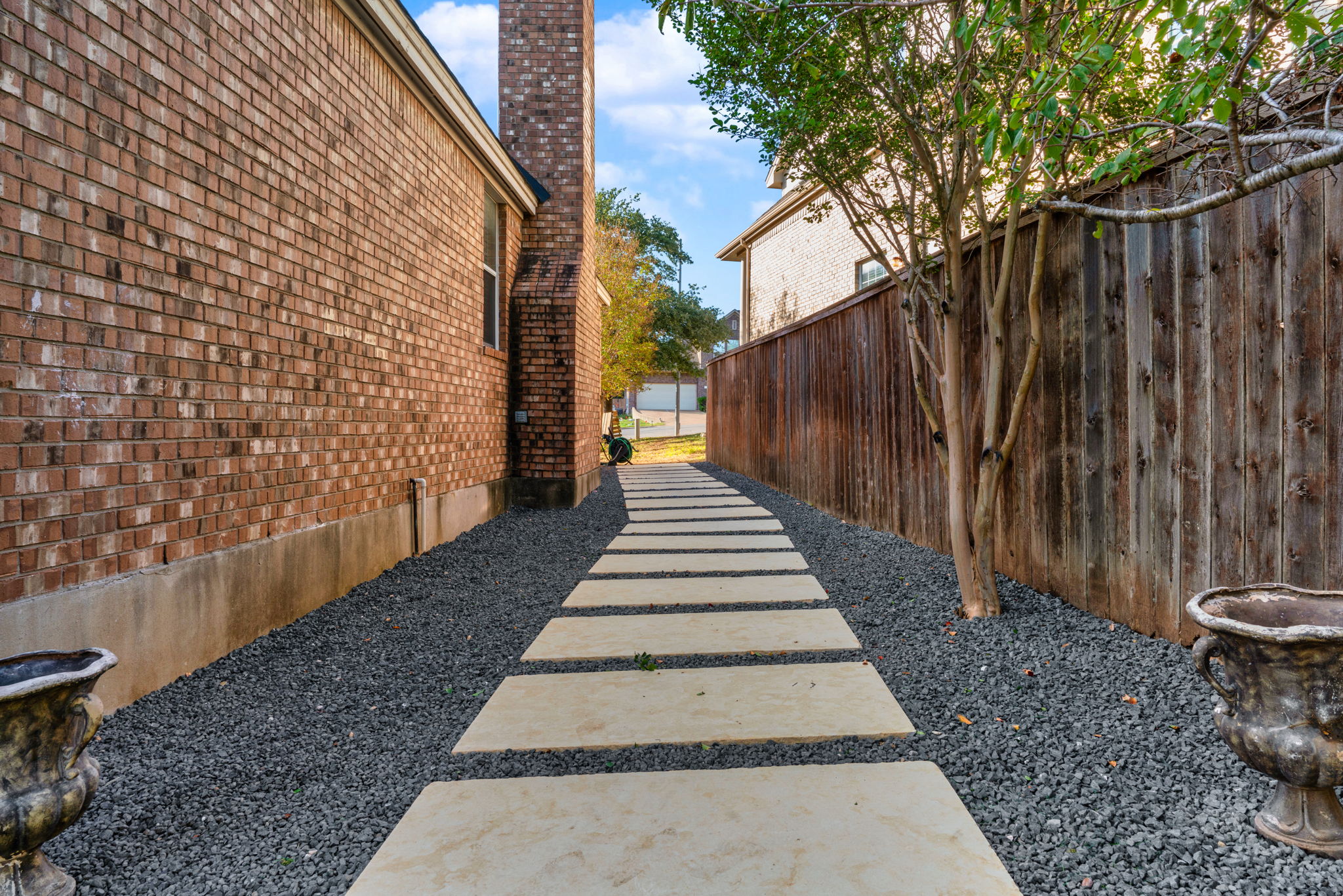 a stone walkway leading from a driveway on the other side of a white privacy fence