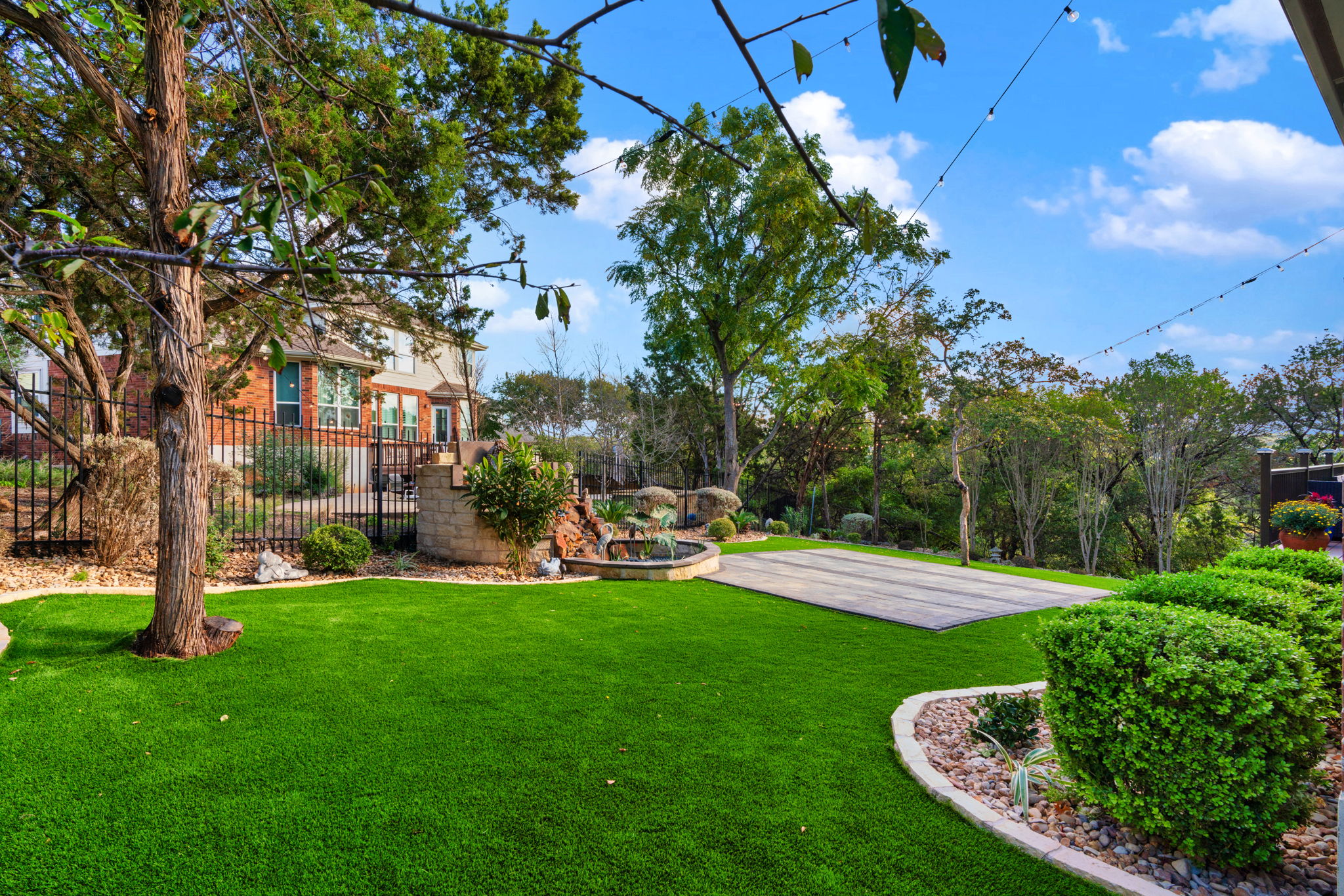 a large backyard with a wrought iron fence, stone zen garden, paver patio, and landscaping