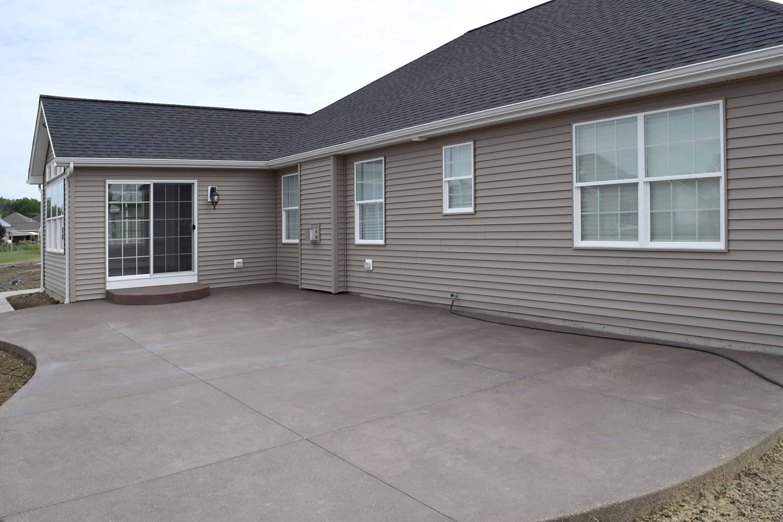 a newly constructed concrete driveway with no landscaping in front of a brown house
