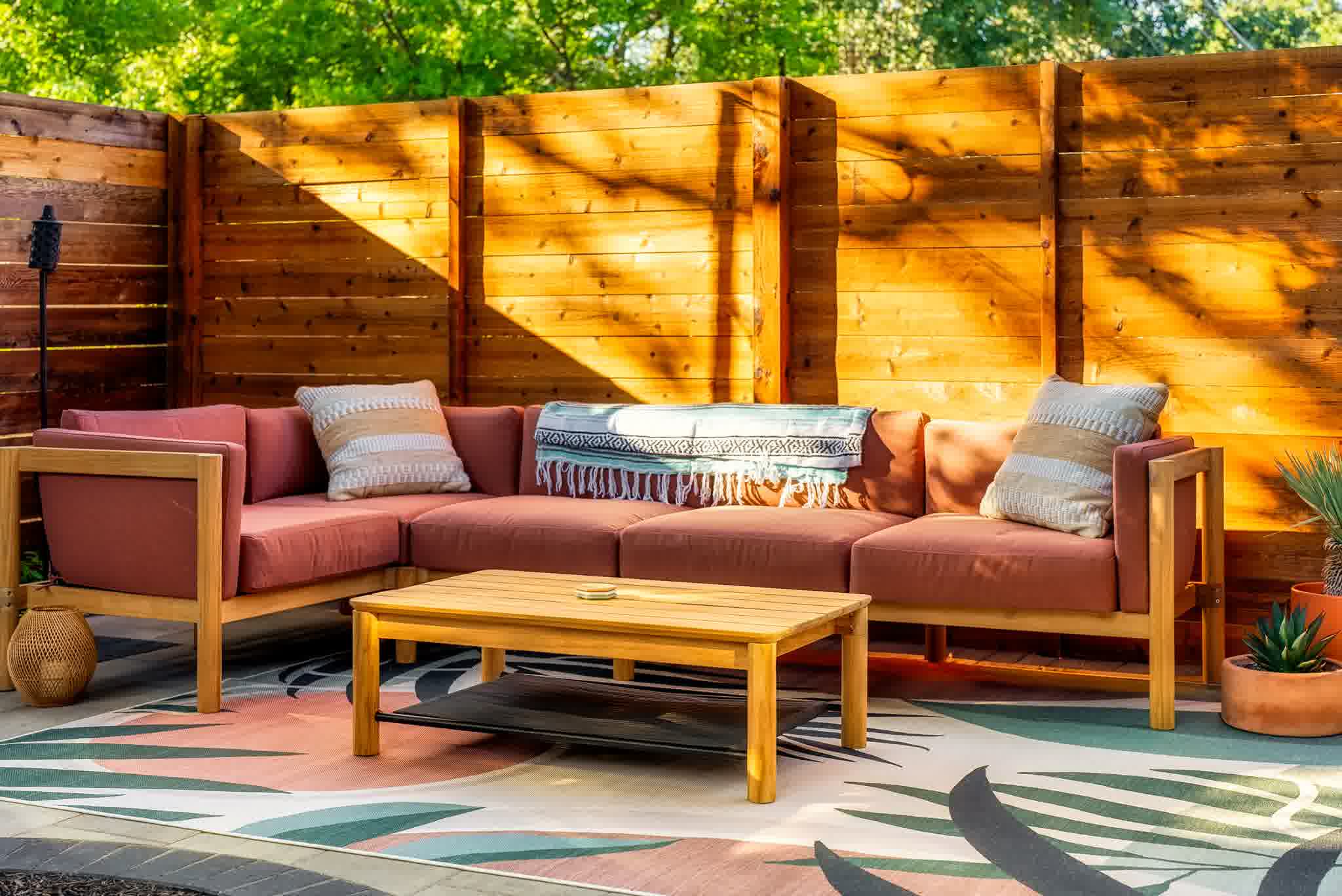 Modern wooden privacy fence surrounding a patio with outdoor sofa, coffee table, and colorful rug under warm sunlight.