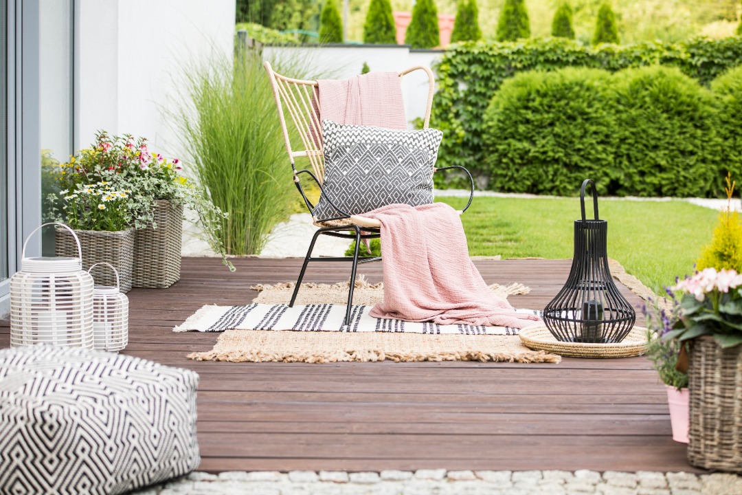 Small backyard deck with stylish chair, patterned rugs, lanterns, and potted plants, creating a cozy garden lounging area.